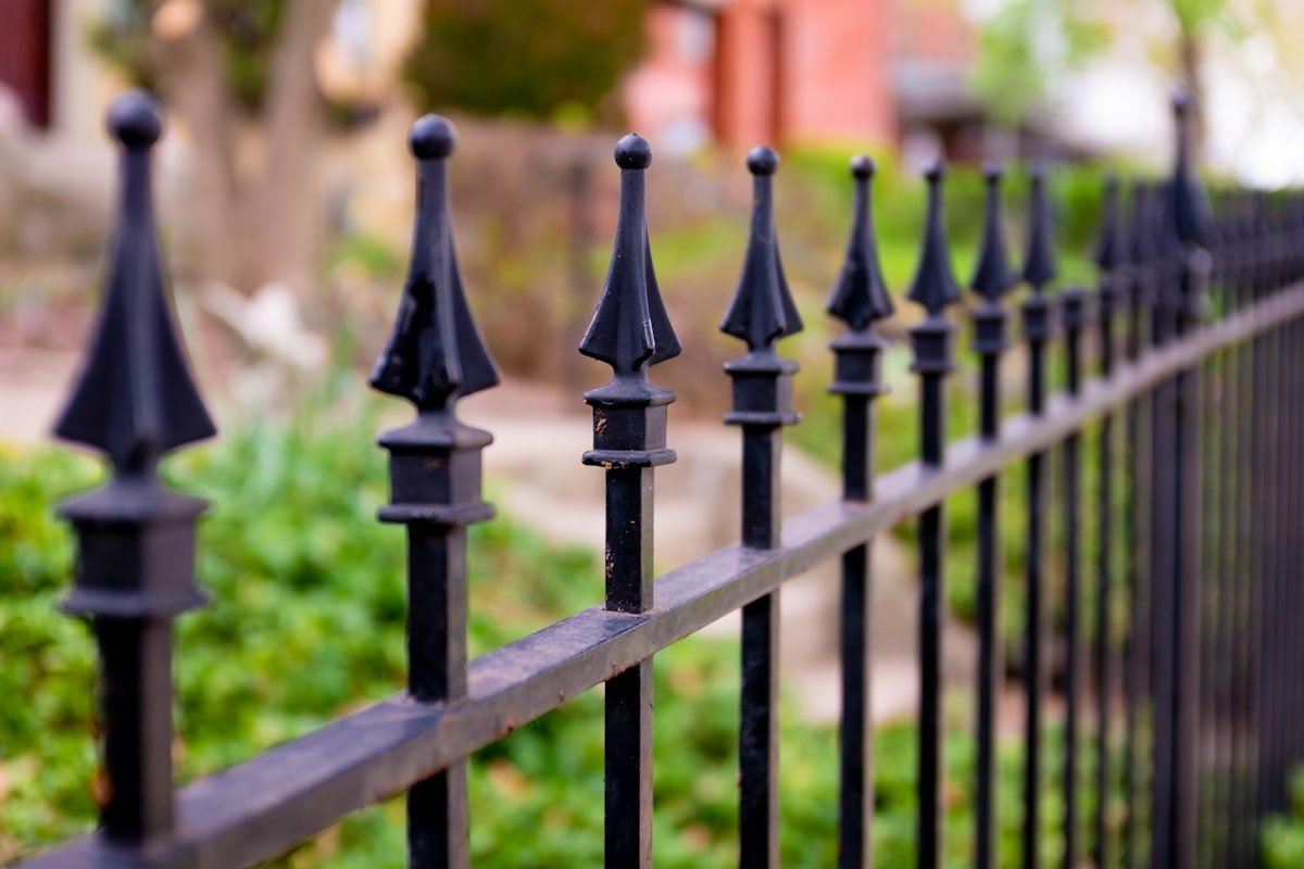 Ornamental black metal fence with decorative finials in front of green landscaping