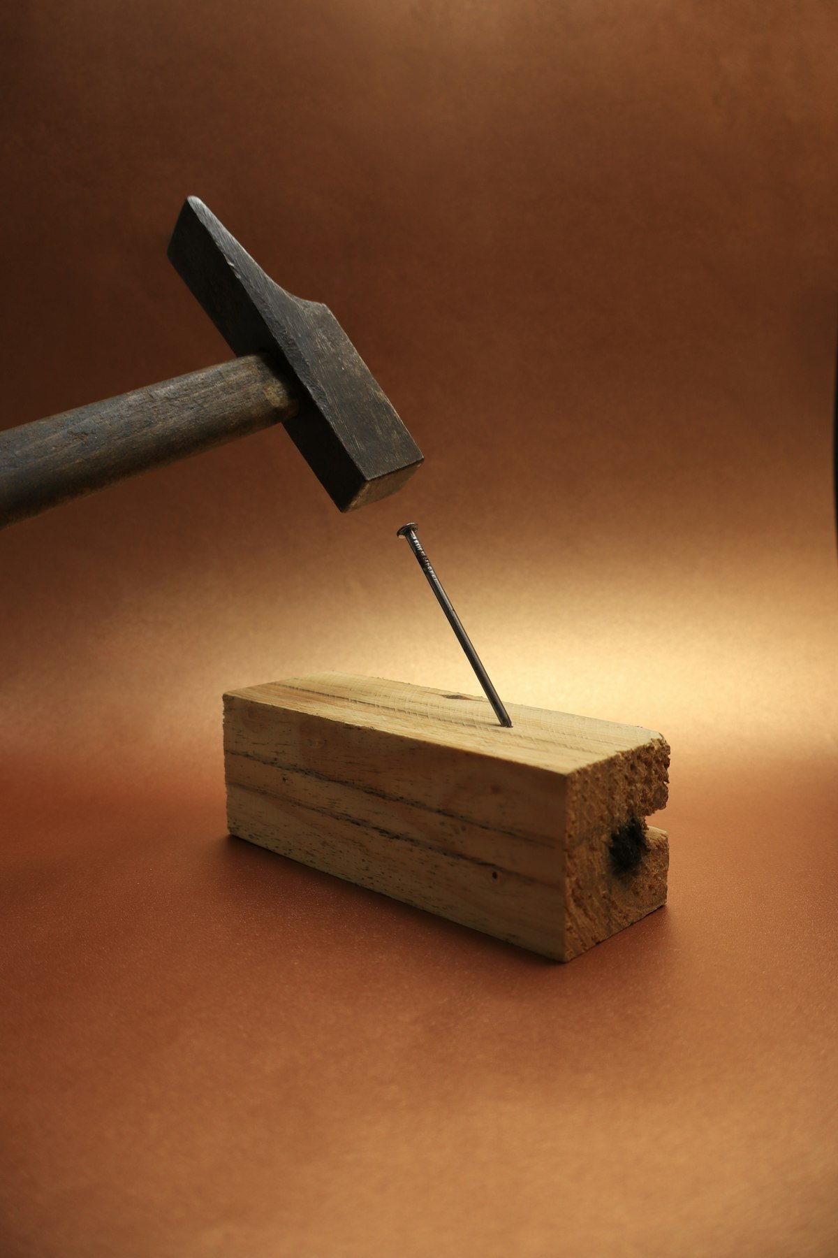 Hammer driving a nail into a wood board, illustrating attaching fence pickets to rails